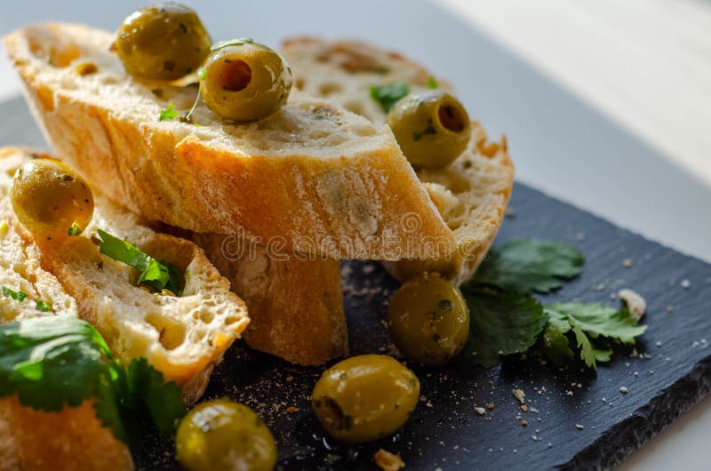 Baguette imbottite di olive, tagliate con olive verdi fresche e prezzemolo, servite su una piastra di pietra fotografia stock libera da diritti