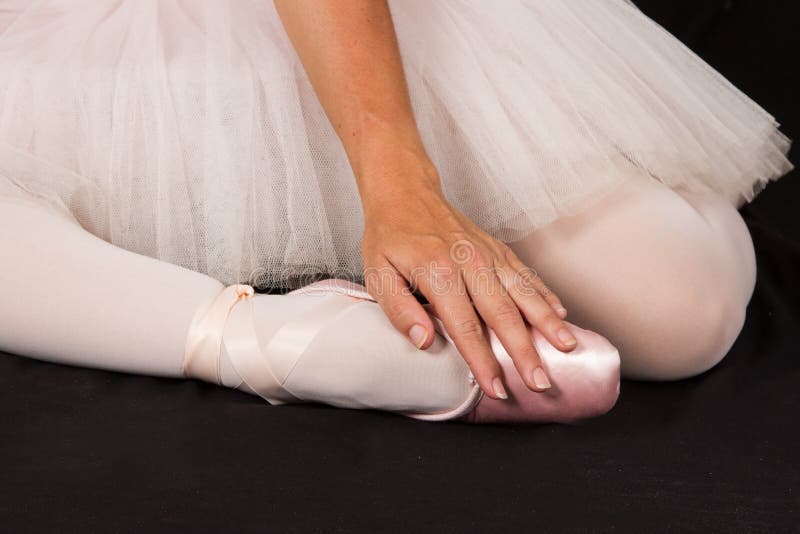 A bailarina senta-se para baixo no assoalho para pôr sobre deslizadores com mãos para o pe imagem de stock A bailarina senta-se para baixo no assoalho para pôr sobre deslizadores com mãos para o pe imagem de stock