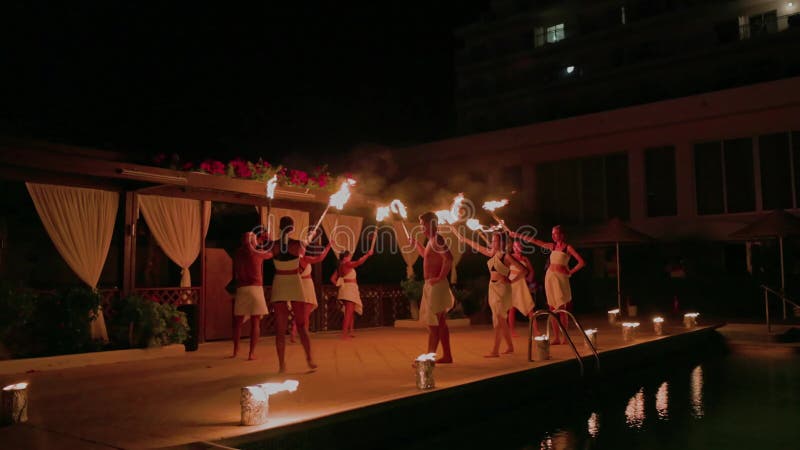 Bailarinas de fuego actuando junto a la piscina en el complejo tropical por la noche vestidas con atuendos tradicionales y sosteni almacen de metraje de vídeo