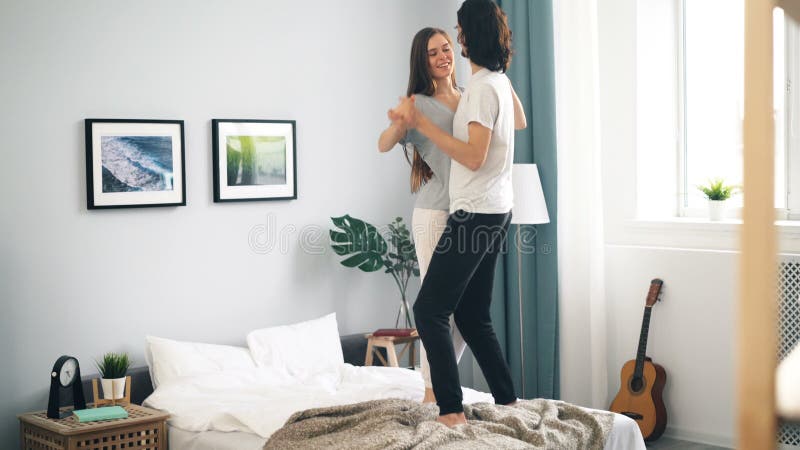 Baile cariñoso adorable de los pares en la cama en casa que abraza divirtiéndose