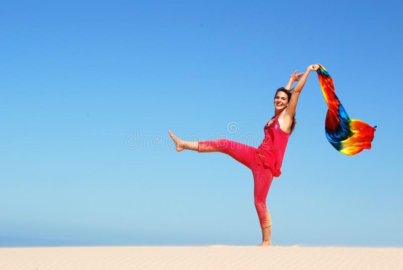 A beautiful active teenage girl in pink clothes holding up a colorful shawl in the wind while dancing on a sand dune in sunshine after arrival on holidays. She has got a happy facial summer expression. A beautiful active teenage girl in pink clothes holding up a colorful shawl in the wind while dancing on a sand dune in sunshine after arrival on holidays. She has got a happy facial summer expression.