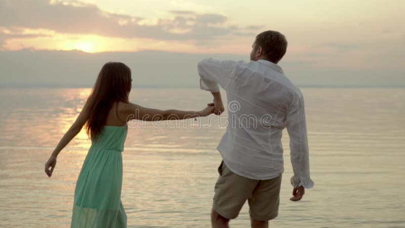 Baile feliz joven de los pares en la playa en la puesta del sol Concepto de amor