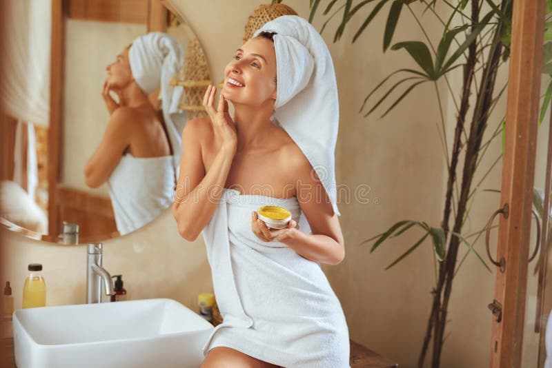Bain femme après. Portrait de serviette de port de modèle heureux après douche. Jeune femelle appliquant la crème anti-âge. images libres de droits