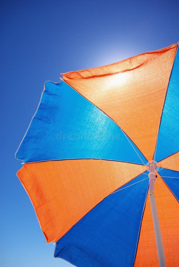 Shade from the hot sun under a colourful blue and orange beach umbrella with blue sky. Shade from the hot sun under a colourful blue and orange beach umbrella with blue sky.