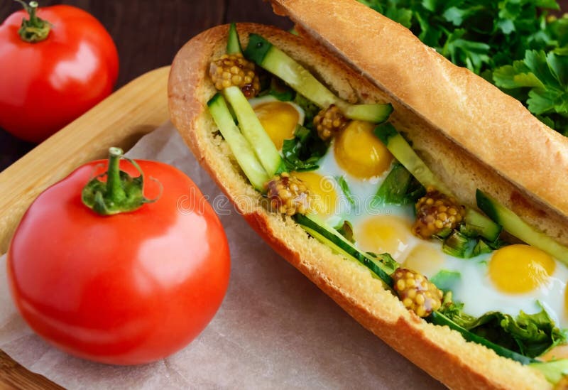 Baked crispy baguette with fried eggs, cucumbers and greens stock image