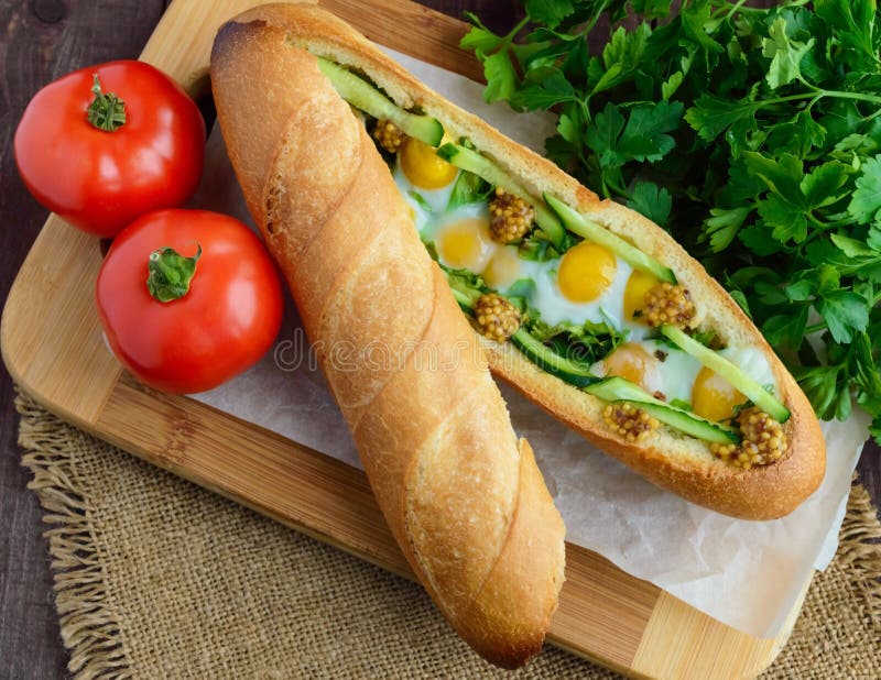 Baked crispy baguette with fried eggs, cucumbers and greens royalty free stock photos