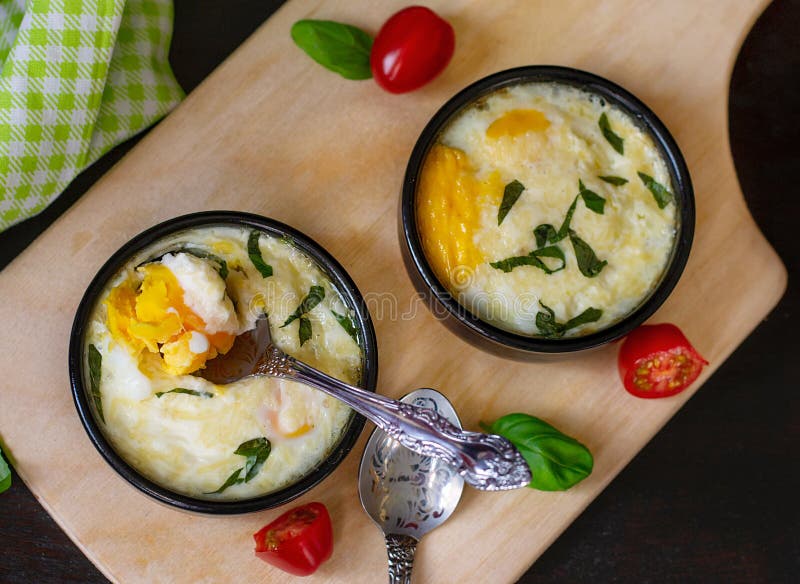 Baked shirred eggs with cheese served with basil for breakfast. Baked shirred eggs with cheese served with basil for breakfast