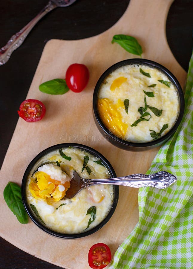 Baked shirred eggs with cheese served with basil for breakfast. Baked shirred eggs with cheese served with basil for breakfast