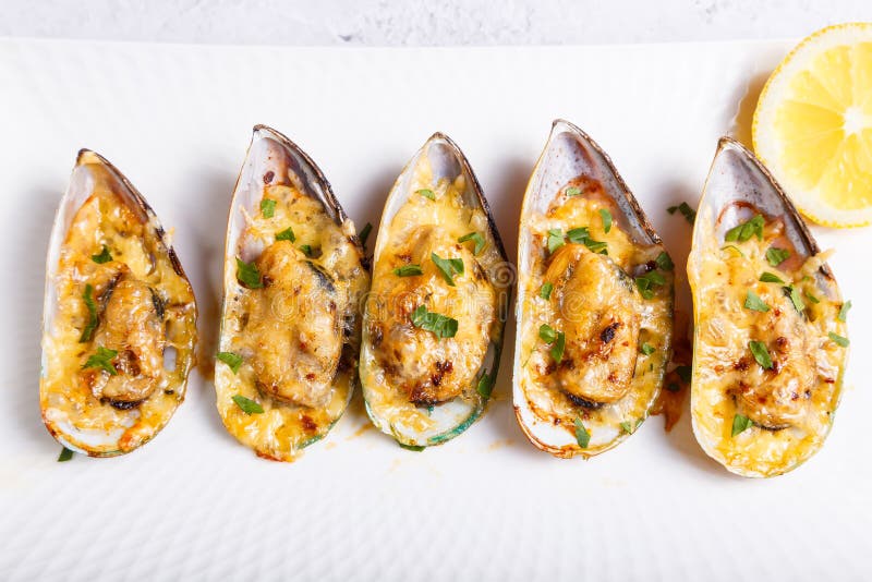 Baked Greenshell mussels in half a shell with cheese, parsley and lemon on a white plate. Traditional hot appetizer. Close-up, top view. Bivalve shell stock images, royalty-free photos and pictures