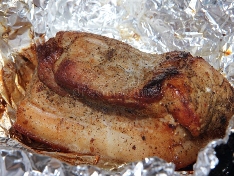 Baked piece of pork meat on aluminum foil, the process of cooking meat dishes in the oven.