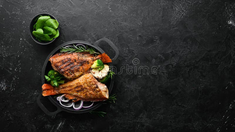 Baked red fish perch with vegetables on a black stone plate. Top view.