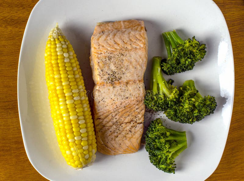 Baked salmon top with black pepper served with corn and broccoli royalty free stock photography