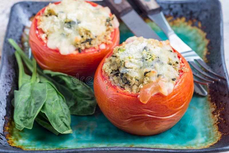 Baked tomatoes stuffed with quinoa and spinach topped with melted cheese on plate, horizontal