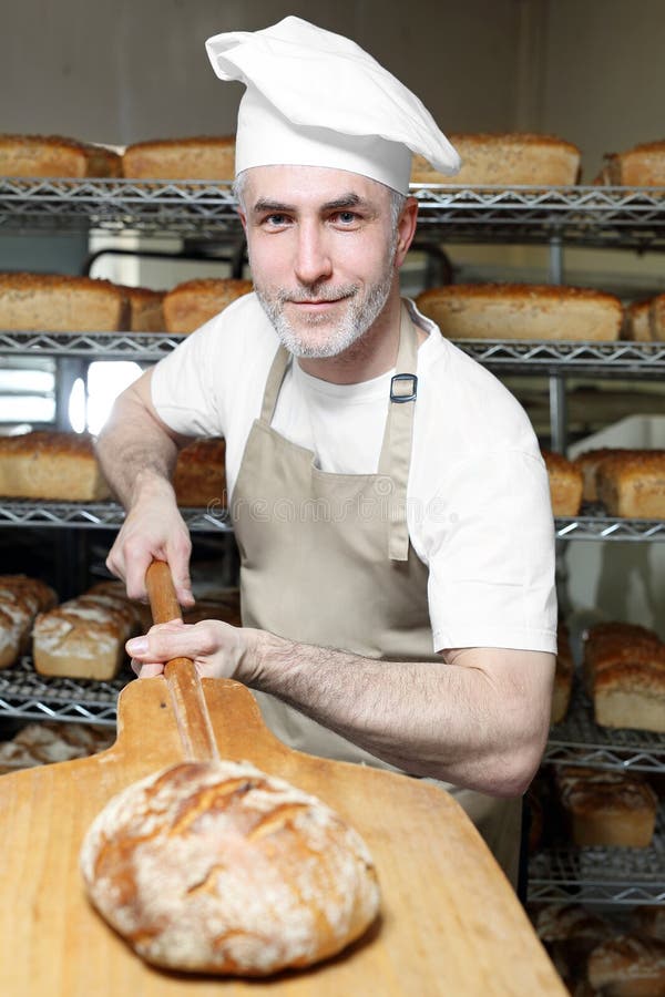 Baker taking out freshly baked bread from the oven of a bakery stock photo