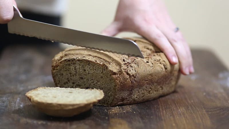 Baker cutting freshly baked loaf of homemade organic sourdough rye bread with bread knife