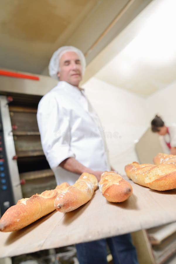 Baker holding five baguettes on paddle.