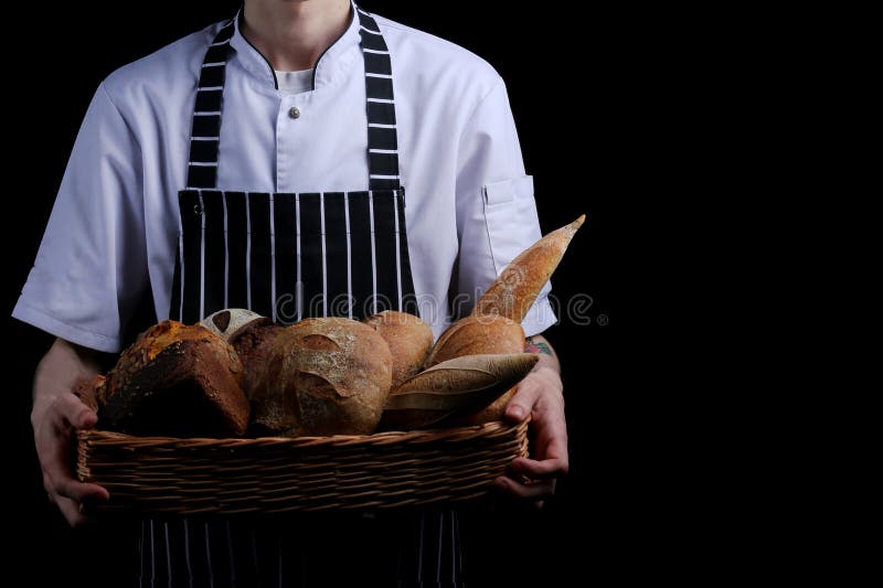 Baker holds basket of bread on black background isolated stock images Baker holds basket of bread on black background isolated stock images