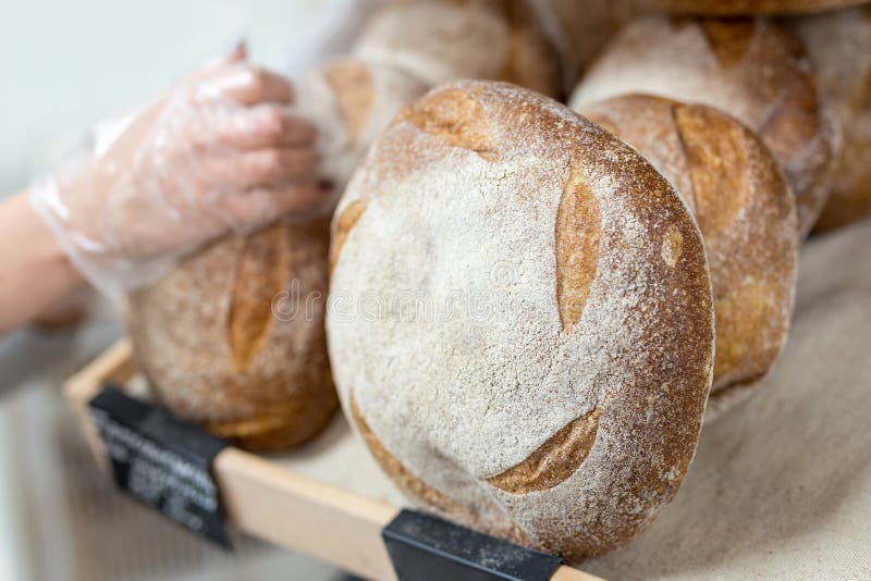 Baker& x27;s hand putting Loafs of warm tasty freshly baked bread in a bakery shop or market stock photo Baker& x27;s hand putting Loafs of warm tasty freshly baked bread in a bakery shop or market stock photo