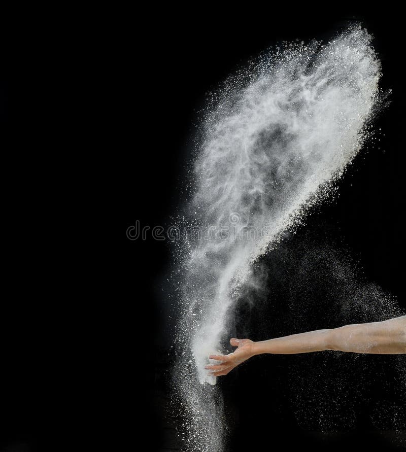 Baker`s hand throws a handful of white wheat flour on a black background