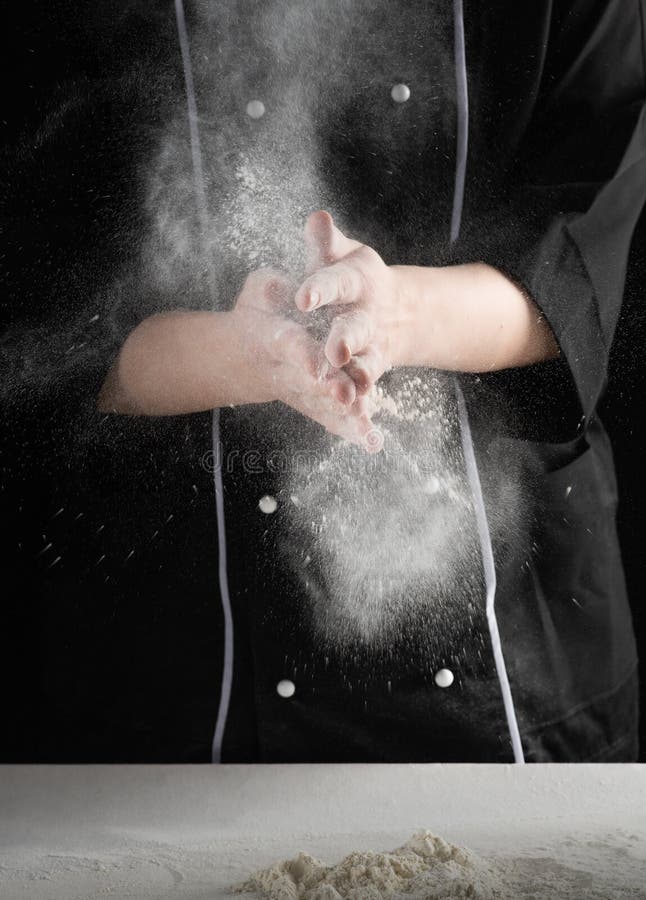 On a dark background baker`s hands sift white wheat flour stock image