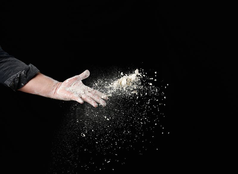 Baker`s male hand throws up a handful of white wheat flour on a black background