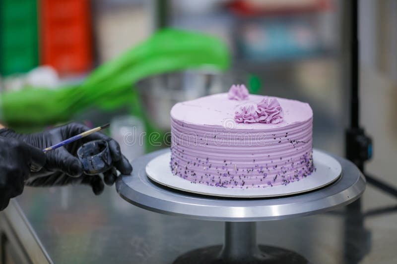 Baker Wearing Protective Gloves Decorating a Beautiful Purple Cake in