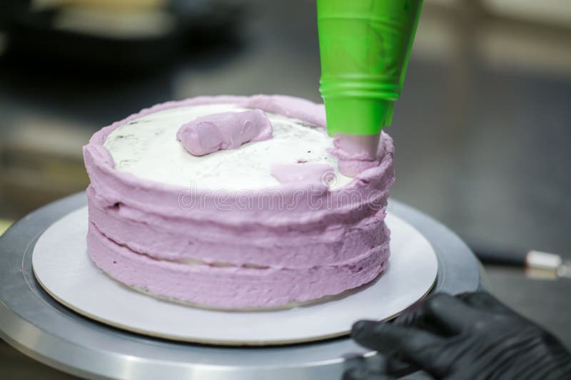 Baker Wearing Protective Gloves Decorating a Beautiful Purple Cake in