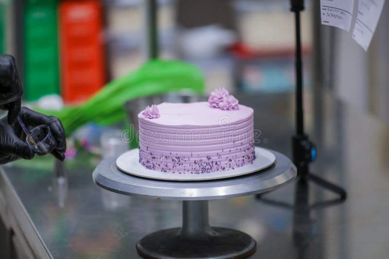 Baker Wearing Protective Gloves Decorating a Beautiful Purple Cake in
