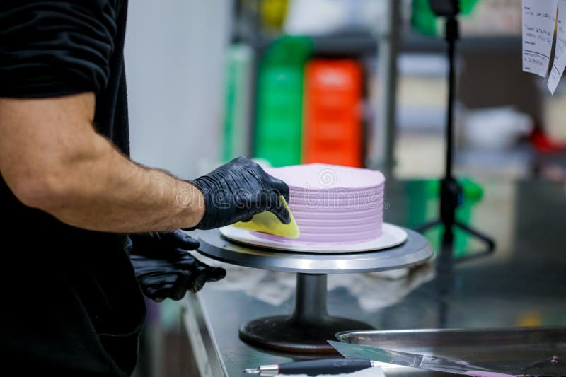 Baker Wearing Protective Gloves Decorating a Beautiful Purple Cake in