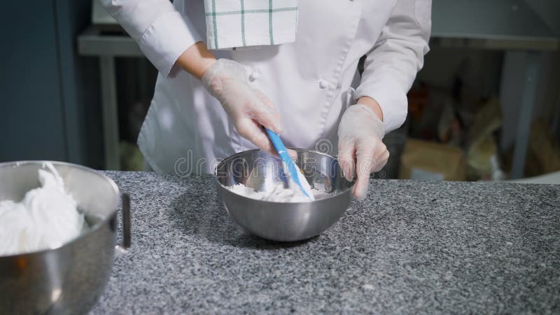 Baker αναμιγνύει τη ζύμη σε ένα κύπελλο μετάλλων για την προετοιμασία των νόστιμων μπισκότων Εργαζόμενος κουζινών άσπρο σε ομοιόμ φιλμ μικρού μήκους