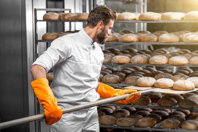 Baker που βάζει με τις φραντζόλες ψωμιού φτυαριών στην κατασκευή στοκ φωτογραφίες
