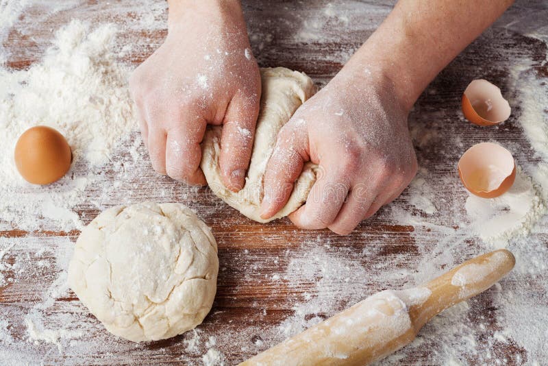 Baker προετοιμάζει τη ζύμη σε έναν ξύλινο πίνακα, τα αρσενικά χέρια ζυμώνουν τη ζύμη με το αλεύρι στοκ φωτογραφία Baker προετοιμάζει τη ζύμη σε έναν ξύλινο πίνακα, τα αρσενικά χέρια ζυμώνουν τη ζύμη με το αλεύρι στοκ φωτογραφία