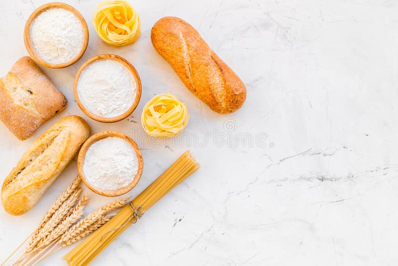 Bakery production, making bread and pasta. Fresh bread and raw pasta near flour in bowl and wheat ears on white stone.