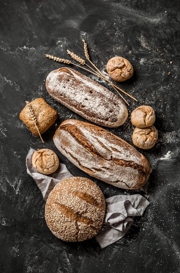 Bakery - gold rustic crusty loaves of bread and buns on black chalkboard background. Still life captured from above top view, flat lay. Bakery - gold rustic crusty loaves of bread and buns on black chalkboard background. Still life captured from above top view, flat lay.