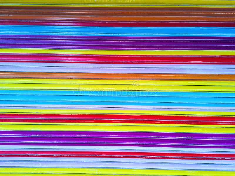 Bright multicolored painted metal roller blinds background. Colorful stripes texture closed corrugated shutters door. Close up metallic lines pattern rolling garage gate. Industrial iron front doorway. Bright multicolored painted metal roller blinds background. Colorful stripes texture closed corrugated shutters door. Close up metallic lines pattern rolling garage gate. Industrial iron front doorway