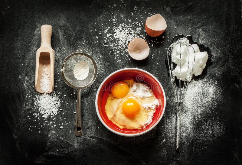 Baking cake ingredients - bowl, flour, eggs, egg whites foam, eggbeater and eggshells on black chalkboard from above. Baking cake ingredients - bowl, flour, eggs, egg whites foam, eggbeater and eggshells on black chalkboard from above.