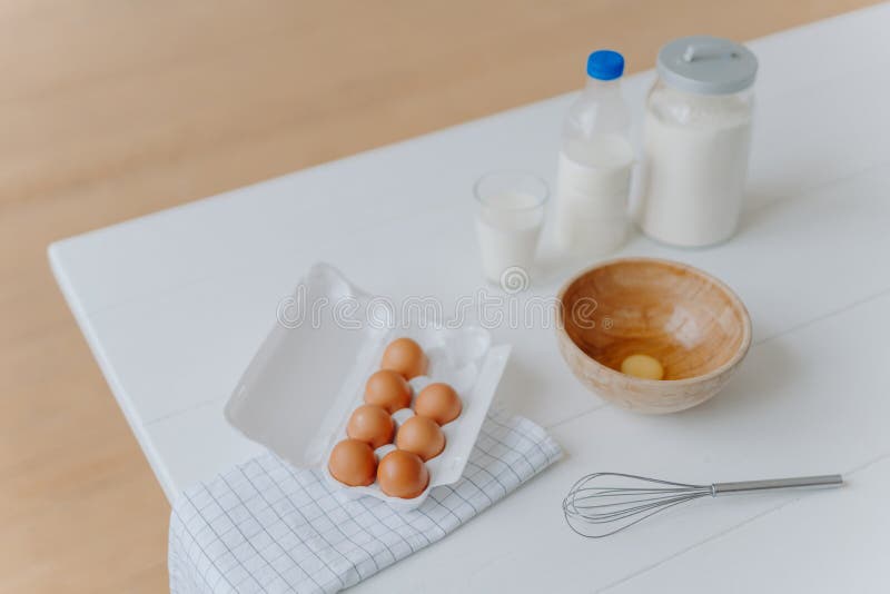 Baking Ingredients on White Table. Eggs, Milk and Flour in Containers. Beater for Whisking and