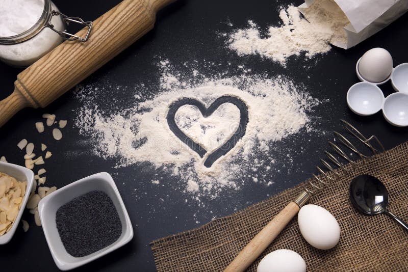 Baking love. Bakery background. Baking ingredients and kitchen utensils on the black background. Flour, almond nuts, eggs. Top