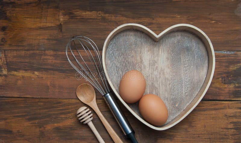 Baking tools with Wooden Heart Shape box with Eggs. Bake or food Background. Dark rustic Wooden Background with copy space. Flat L