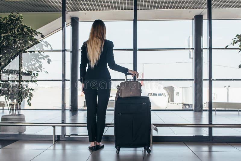 Bakre sikt av det slanka unga kvinnliga handelsresandeanseendet i hållande tunga resväskor för flygplatsterminal som ser till och royaltyfri foto Bakre sikt av det slanka unga kvinnliga handelsresandeanseendet i hållande tunga resväskor för flygplatsterminal som ser till och royaltyfri foto