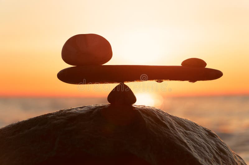 in the balance of power - natural scales of stones by the sea to the orange sunset