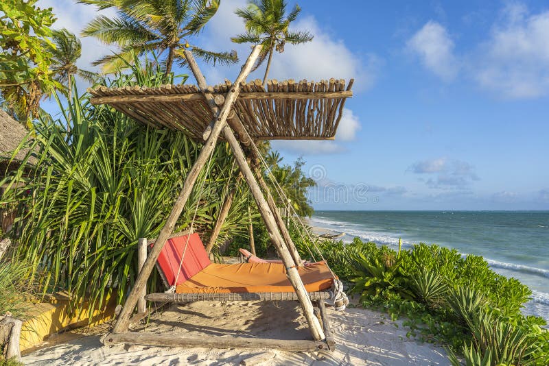 Wooden swing with a mattress under a canopy on the tropical beach near sea, island Zanzibar, Tanzania, East Africa, travel and vacation concept. Wooden swing with a mattress under a canopy on the tropical beach near sea, island Zanzibar, Tanzania, East Africa, travel and vacation concept