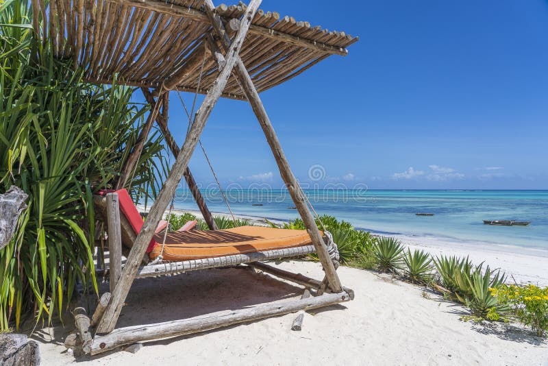 Wooden swing with a mattress under a canopy on the tropical beach near sea, island Zanzibar, Tanzania, East Africa, travel and vacation concept. Wooden swing with a mattress under a canopy on the tropical beach near sea, island Zanzibar, Tanzania, East Africa, travel and vacation concept