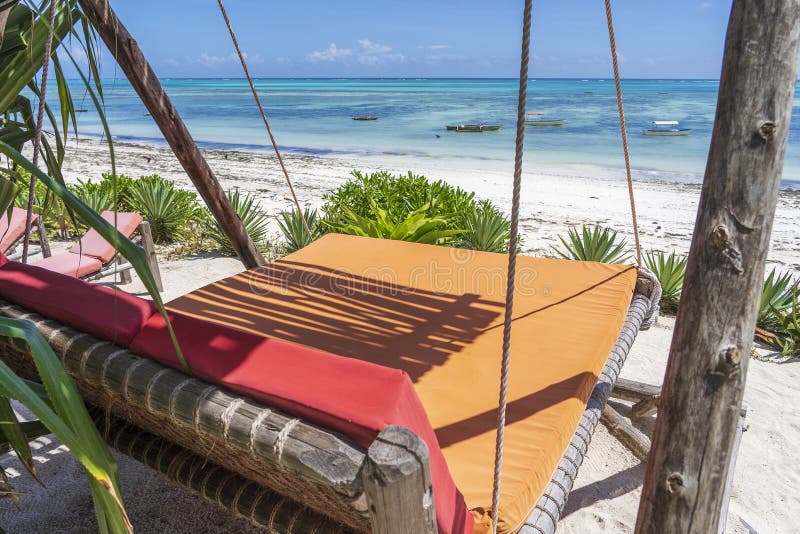 Wooden swing with a mattress under a canopy on the tropical beach near sea, island Zanzibar, Tanzania, East Africa, travel and vacation concept. Wooden swing with a mattress under a canopy on the tropical beach near sea, island Zanzibar, Tanzania, East Africa, travel and vacation concept