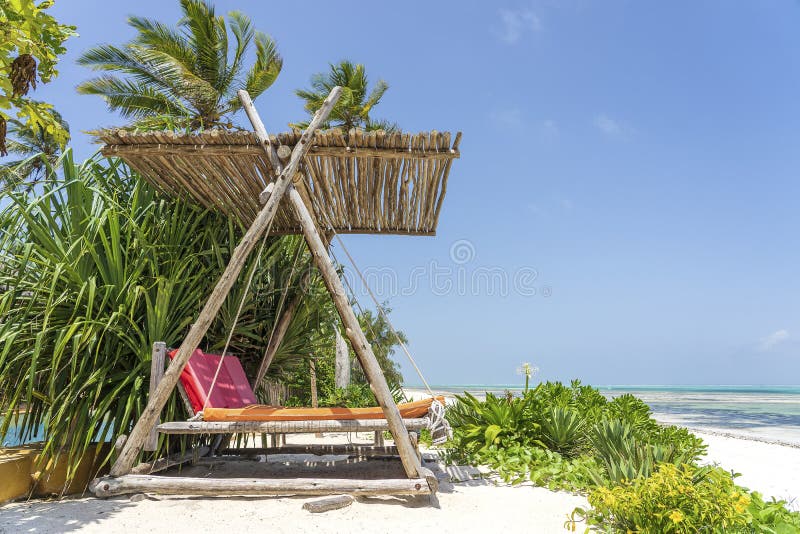 Wooden swing with a mattress under a canopy on the tropical beach near sea, island Zanzibar, Tanzania, East Africa, travel and vacation concept. Wooden swing with a mattress under a canopy on the tropical beach near sea, island Zanzibar, Tanzania, East Africa, travel and vacation concept