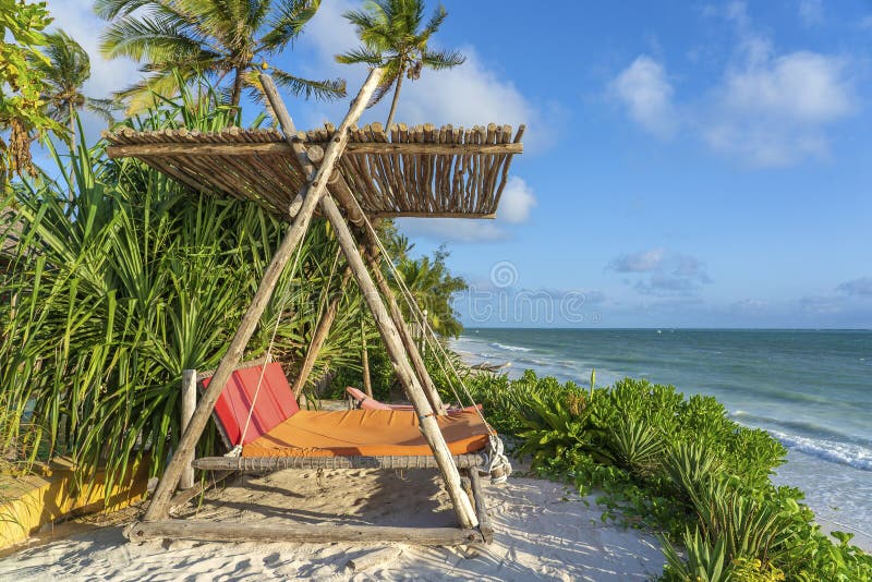 Wooden swing with a mattress under a canopy on the tropical beach near sea, island Zanzibar, Tanzania, East Africa, travel and vacation concept. Wooden swing with a mattress under a canopy on the tropical beach near sea, island Zanzibar, Tanzania, East Africa, travel and vacation concept