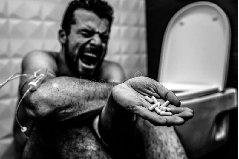 Balck and white picture of young man screaming and yelling on floor in rest room. He suffer. Guy show pills in hand royalty free stock photography Balck and white picture of young man screaming and yelling on floor in rest room. He suffer. Guy show pills in hand royalty free stock photography