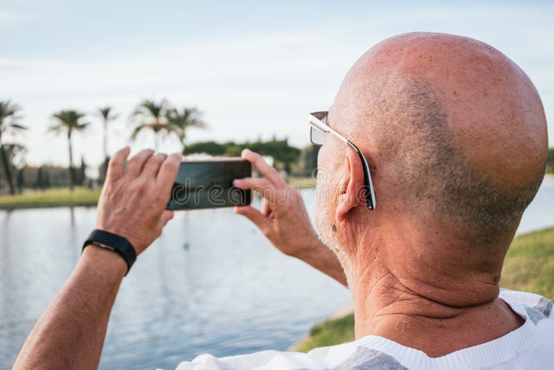 65-year-old man taking a photo with a smartphone in a park