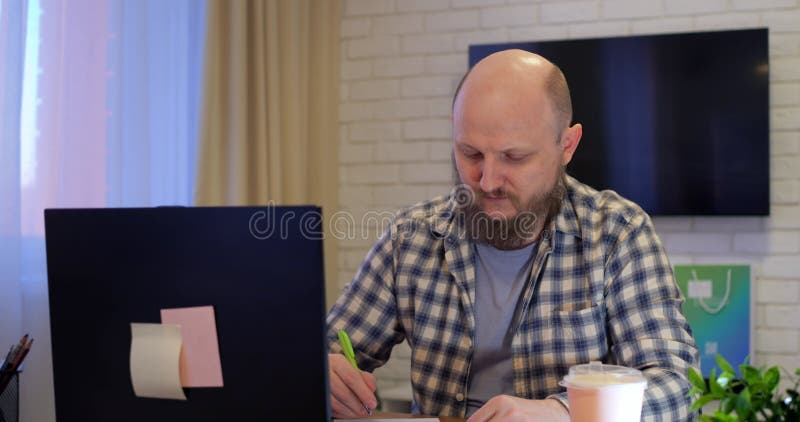 Bald-man öppnar en bärbar dator och börjar arbeta på matbordet hemma i rum under karantänen. Arbeta hemma under lager videofilmer