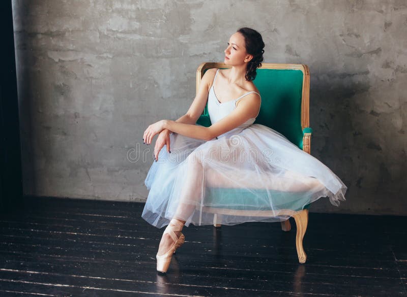 The Ballet dancer ballerina in beautiful light blue dress tutu skirt posing sitting on vinage chair in loft studio. The Ballet dancer ballerina in beautiful light blue dress tutu skirt posing sitting on vinage chair in loft studio